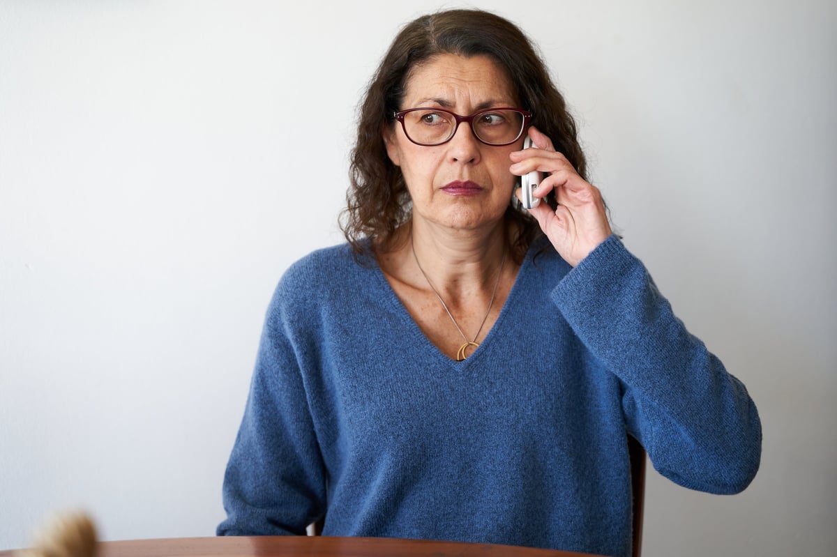 Senior phone fraud concept — mature woman distrusting a phone call