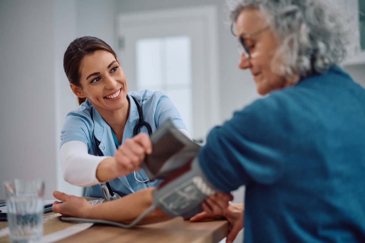 Happy visiting nurse checking blood pressure of a senior woman at home.