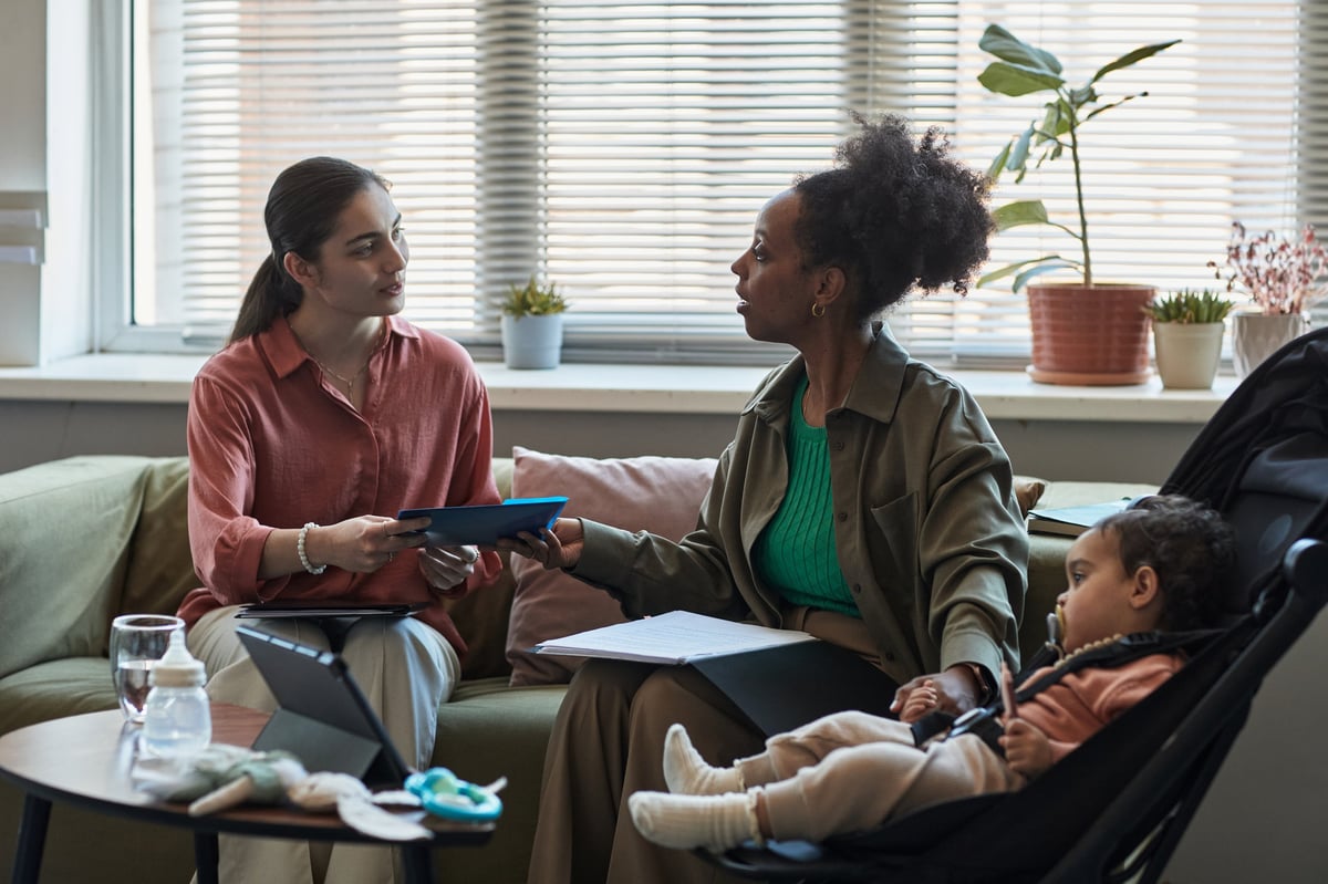 Two women engaging in conversation while sitting on a couch in a living room, one woman holding a tablet, planning care together