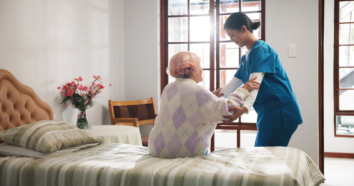 Senior woman, caregiver and help on bed with care, assisted living and support in nursing home