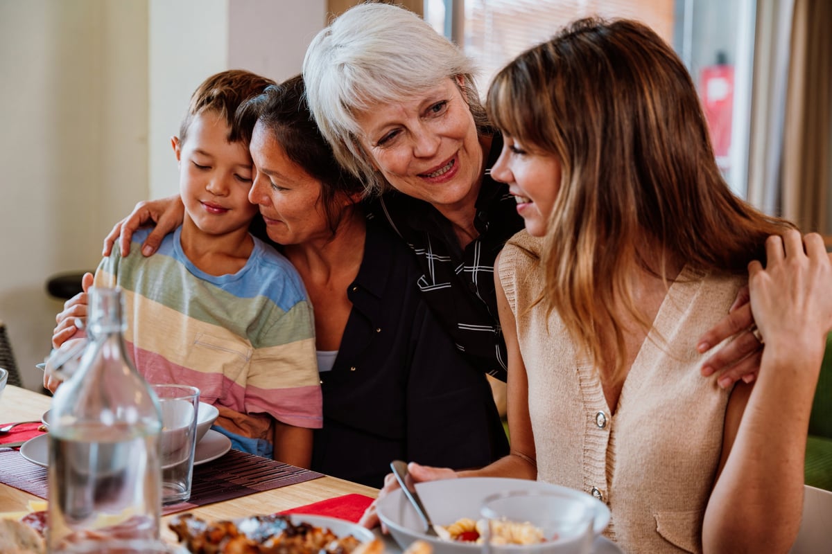 Happy multi-generational family gathering around a dining table, sharing a delicious meal, embracing and laughing with warm smiles