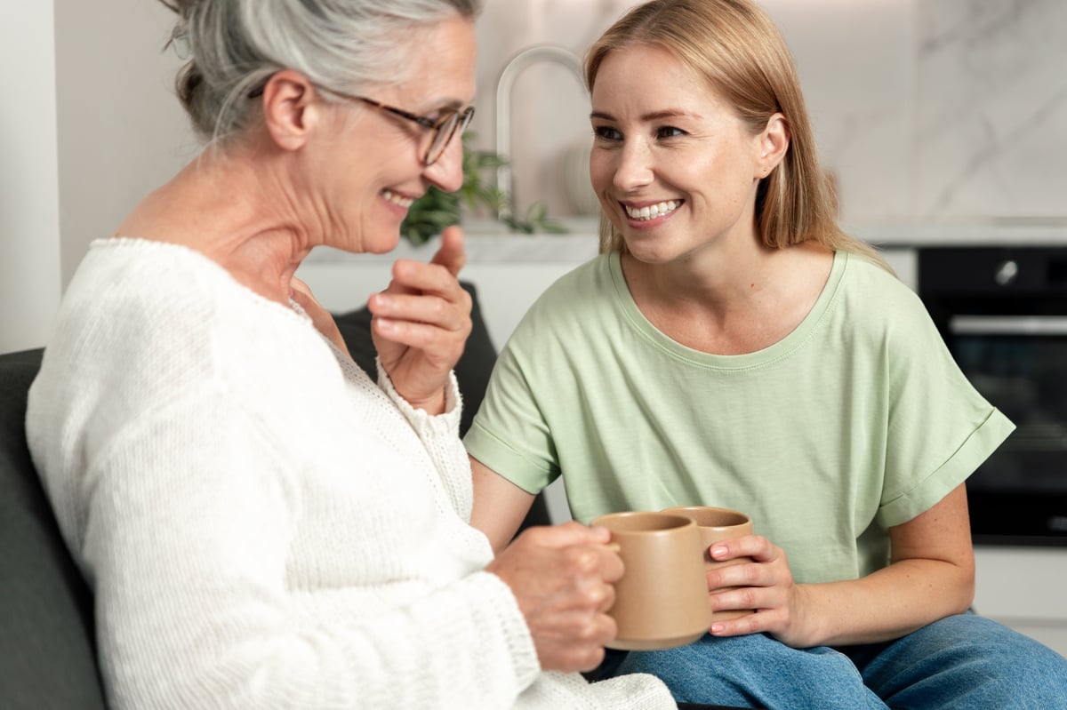Bonding over conversation - an elderly mother and her adult daughter enjoy a cozy afternoon in their living room, sharing smiles and laughter