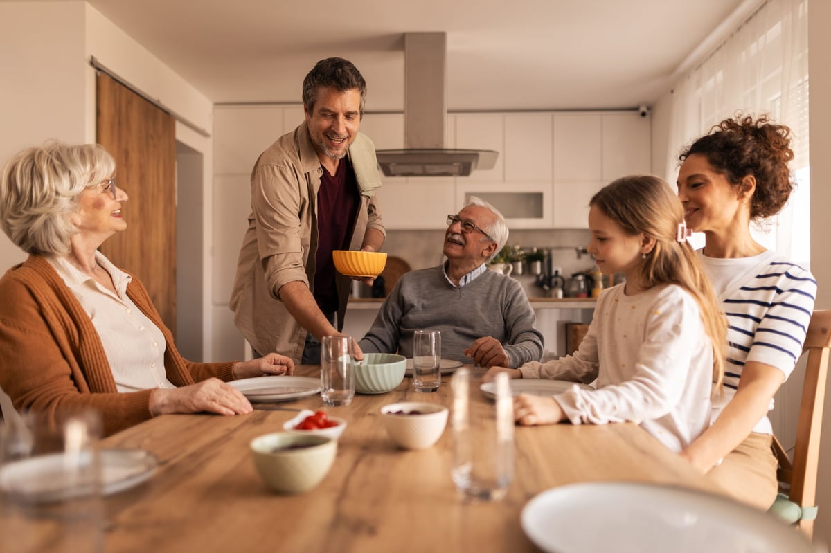 Multi-generation family gathered around a kitchen table sharing a relaxed meal, smiling and connecting across generations