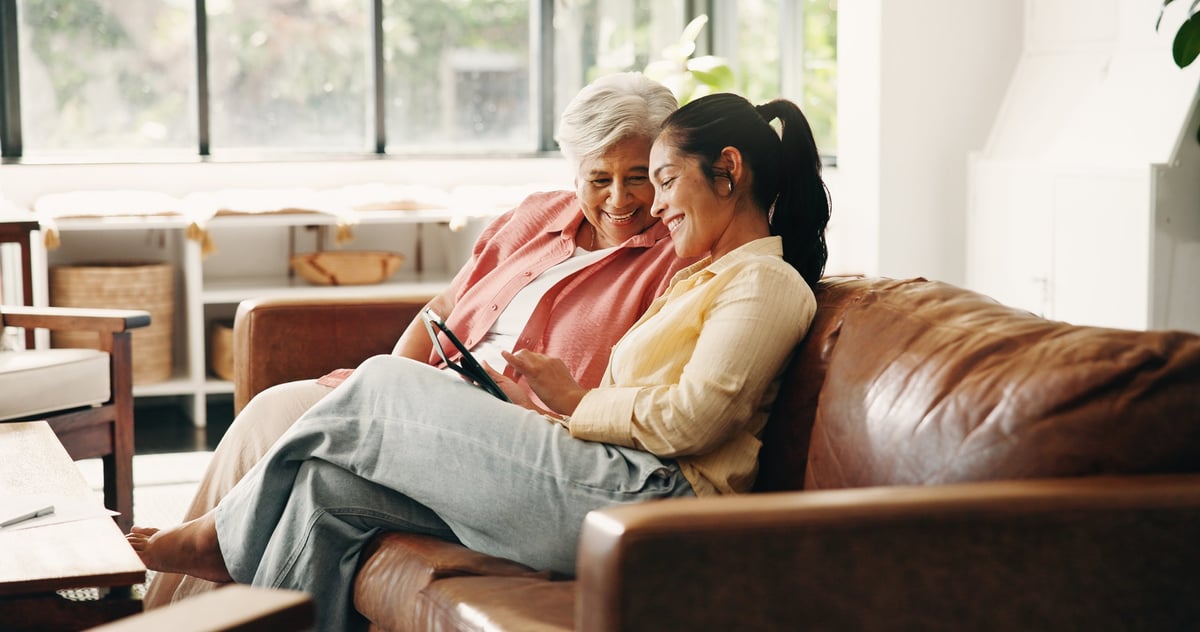 Smile, tablet or visit with old woman and daughter on sofa in home together for bonding or love
