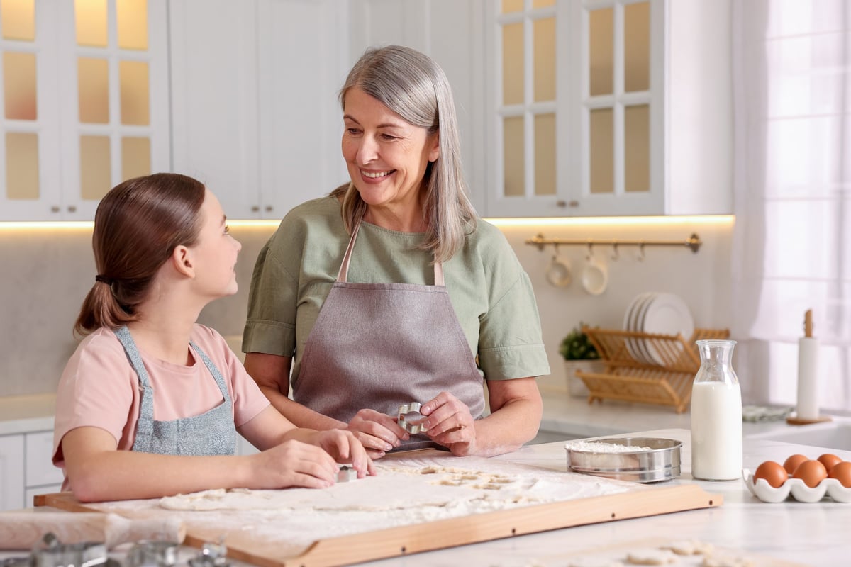 Smiling grandmother and her granddaughter cooking together at table in kitchen